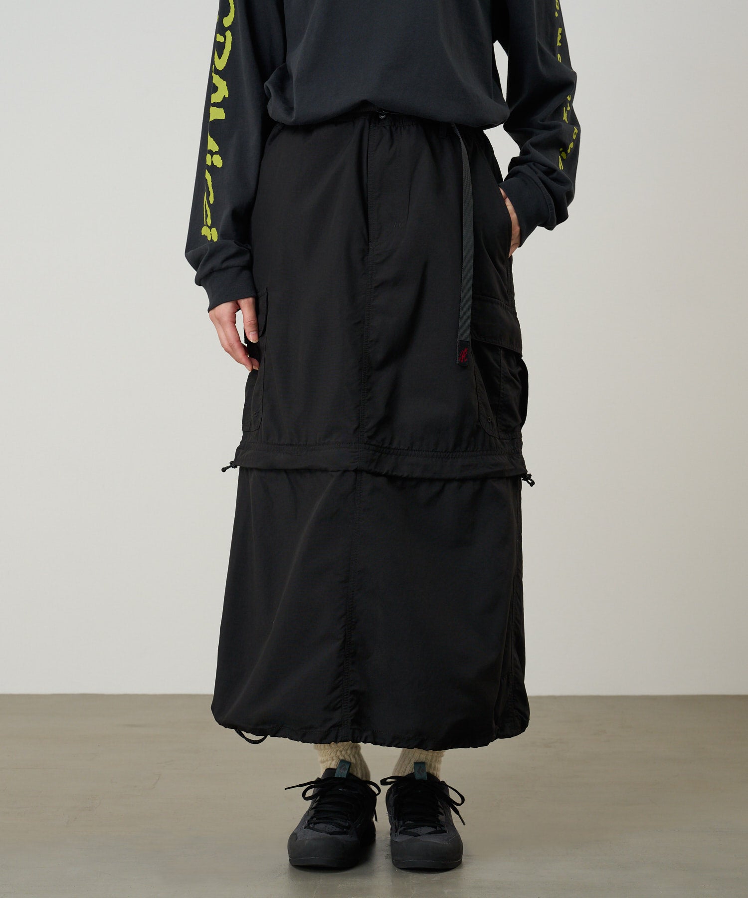 Back view of model wearing Gramicci Convertible Cargo Skirt Black with eco cotton fabric, utility pockets and adjustable everyday design.