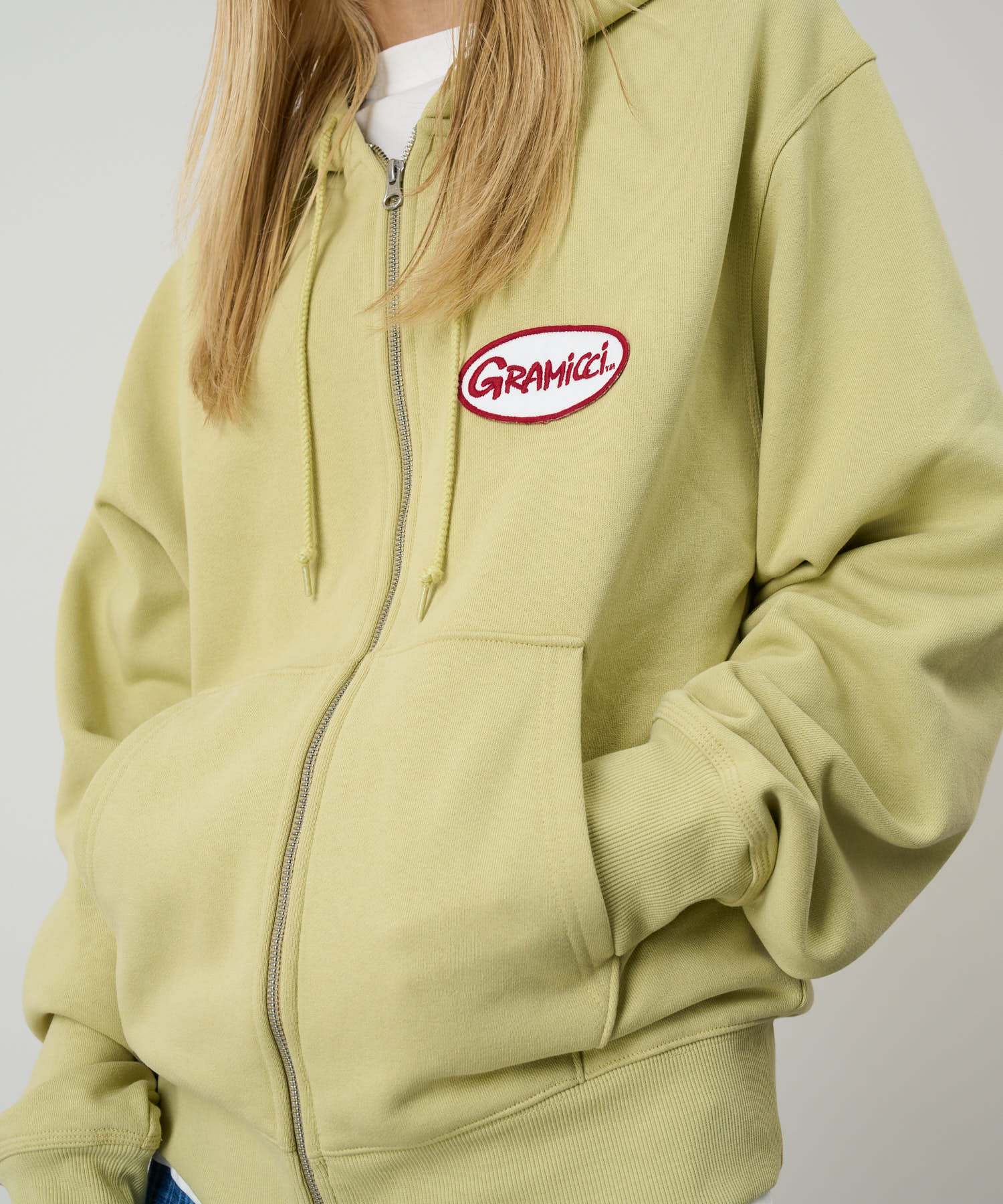 Model wearing Gramicci Oval Patch Zip Hooded Sweatshirt Lime with a soft fleece fabric, full zip and drawstring hood for everyday comfort.
