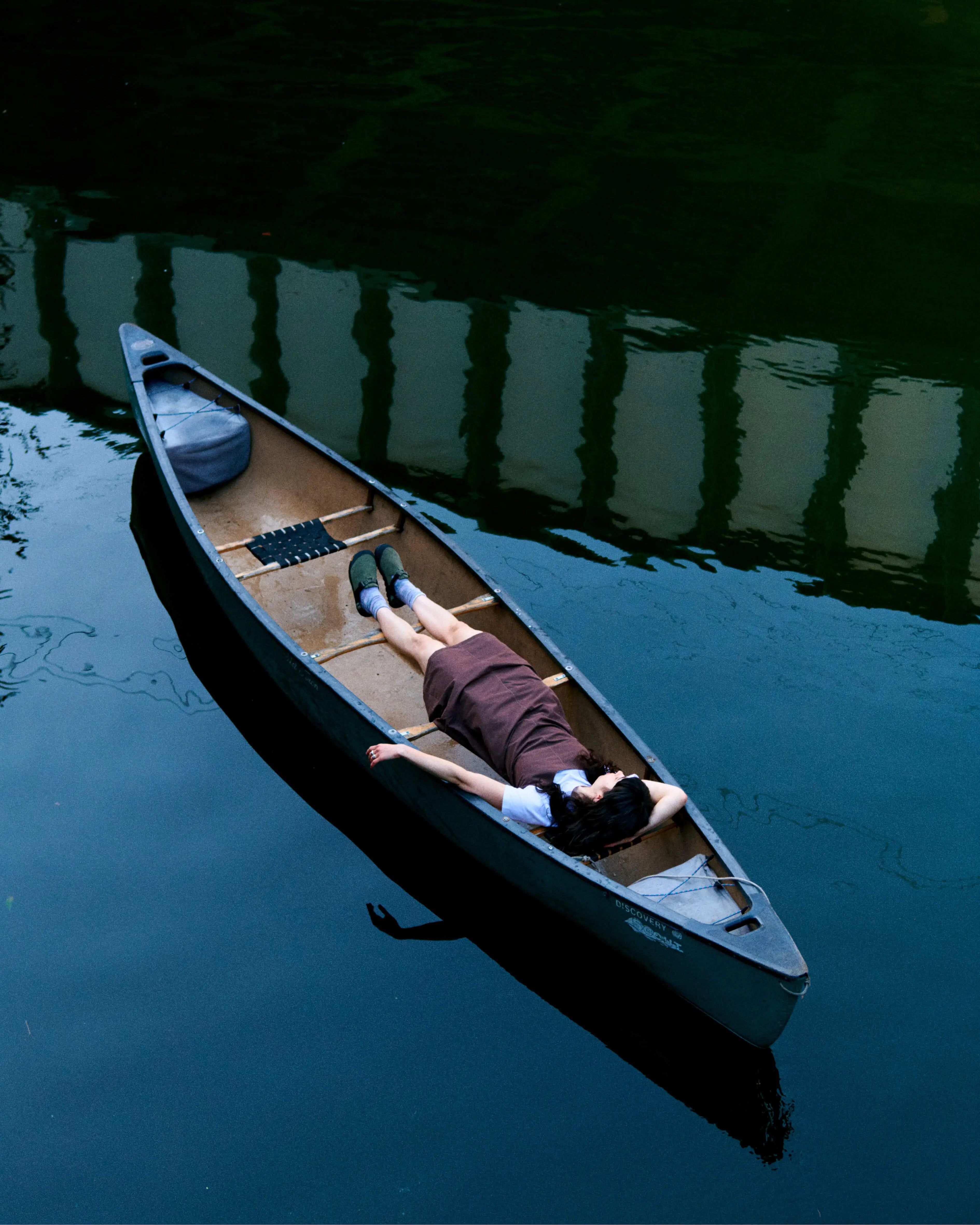 Model in canoe on calm water showing Gramicci SS26 outdoor lifestyle collection.